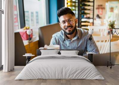 Young asian man with hat using laptop at cafe. Young indian man working on laptop Wall mural